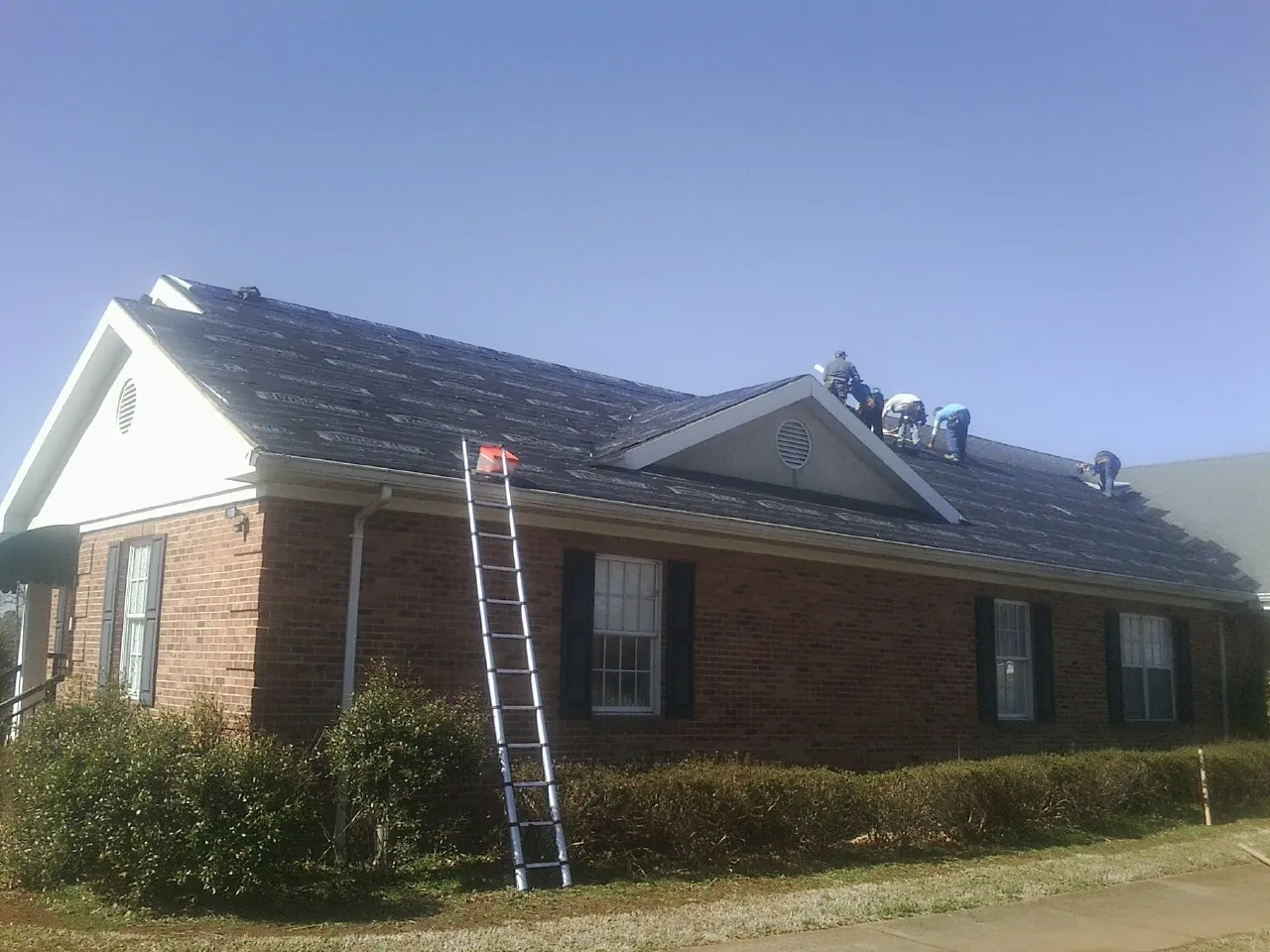 Crew tearing shingles off a brick ranch roof with a ladder set — Metal Roof Repair work by our crew in West Hartford