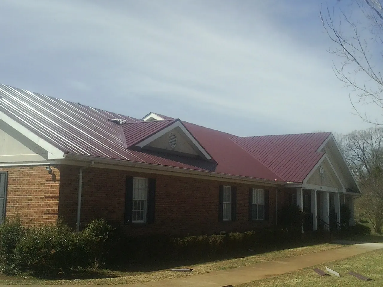 Red metal roof with gabled entries on a long brick building, from a Hail Damage Roof Repair job in West Hartford