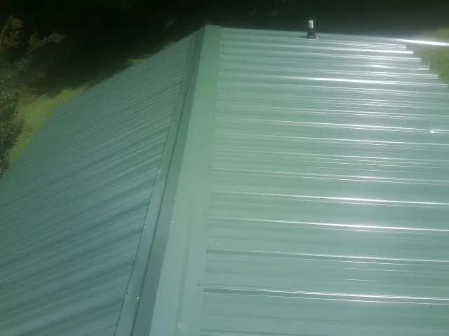 New green metal panels meeting at the ridge of a roof — Flat Roof Repair work by our crew in West Hartford