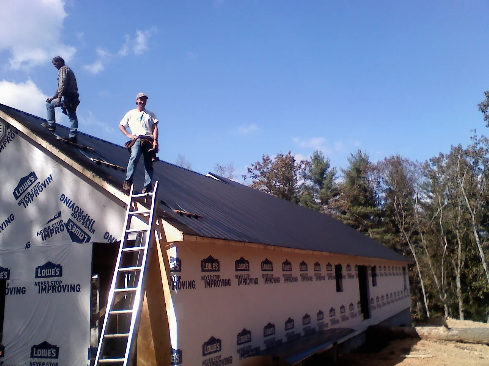 Two roofers standing on a long dark metal roof over a wrapped building in West Hartford
