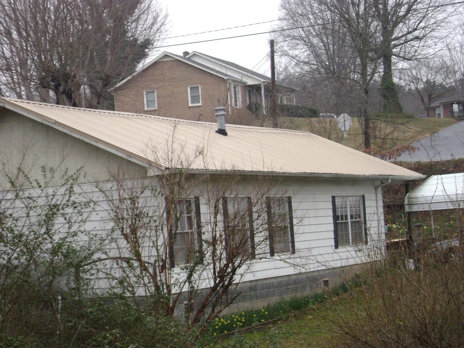 Tan metal roof on a white sided house set into a hillside — Commercial Roofing by Roofing Brothers in West Hartford